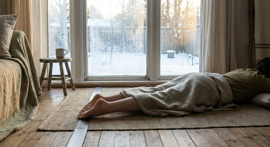 A person resting barefoot on a grounding mat near a frost-covered window with soft winter morning light streaming in.